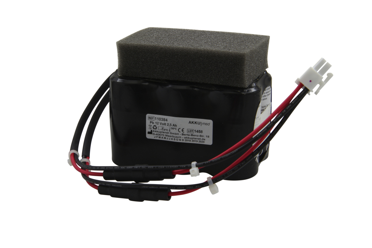 Black, rectangular ‘ AKKUmed ’ lead-acid battery with a dark grey foam pad. Black and red cables, secured with white cable ties, run down the side to a white plastic plug. 12 volts, 2.5 Ah, for DeVilbiss suction pumps.