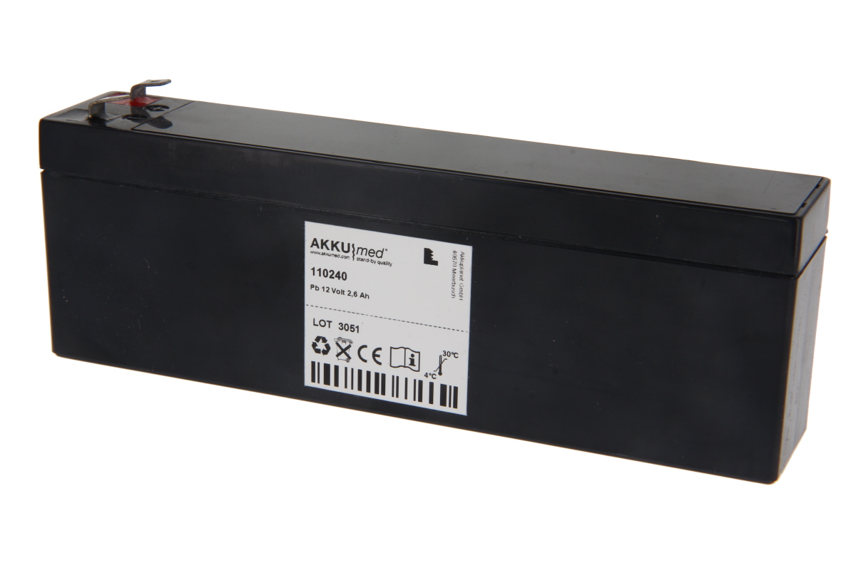 Black rectangular 'AKKUmed' lead-acid battery with white side label. Manufacturer name, 'Pb 12 Volt 2.6 Ah', and symbols incl. CE mark and barcode visible. Terminals on top, one marked red.