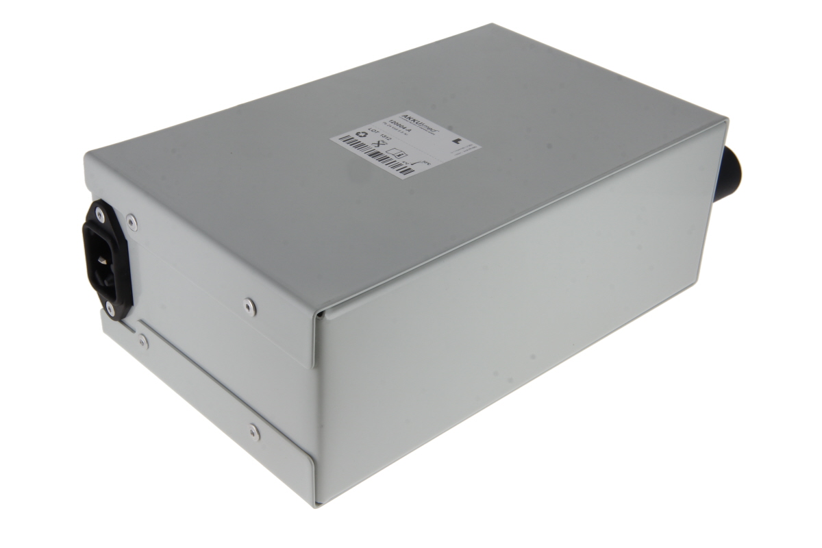 A grey, rectangular ‘ AKKUMED ’ lead-acid battery in a robust metal casing, ideal for ‘ Arjo ’ lifters. A black power connector is visible on the left. On the top is a white label with product information and a barcode.