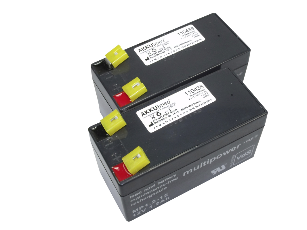 Two identical black AKKUmed lead-acid battery inserts (12 V, 1.2 Ah each) are arranged staggered. Two terminals with red/black caps at top, covered by yellow protective caps. Ideal for hospital beds like Wissner-Bosserhoff Altura/Eleganza.